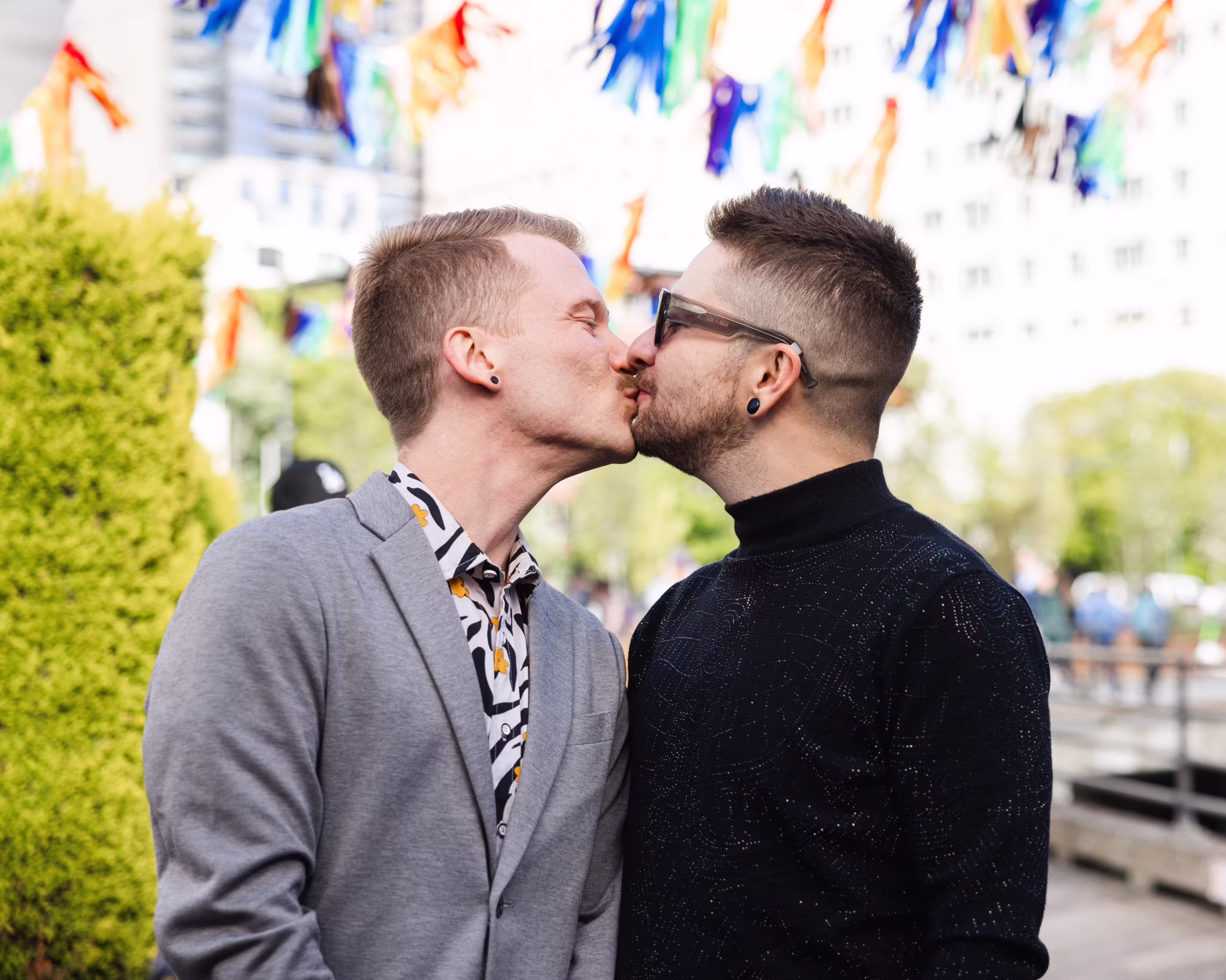 Couple kissing outdoors beneath colorful pride flags